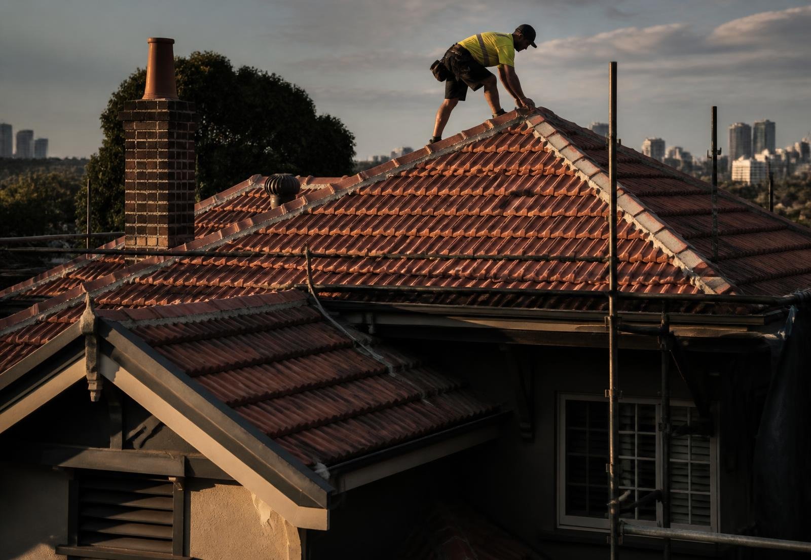 Roofer repointing terracotta ridge capping on a Sydney home at sunset